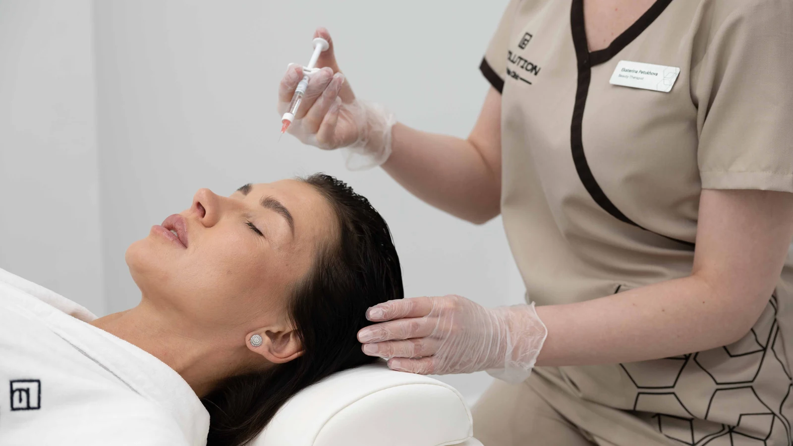 Gloved practitioner holding a syringe above a patient resting on a treatment bed